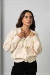 Saco de punto color crema con diseño de flores bordadas en relieve, cuello en V, cierre frontal con botones y mangas largas con puños acanalados.