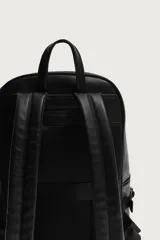 Mochila de acabado liso en color negro, con compartimento principal con cierre de cremallera, bolsillo frontal, detalle de hebillas en los laterales y asas acolchadas.