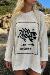 Sweater oversize de tejido de punto color crudo, con cuello redondo, mangas largas y un gran panel rectangular frontal bordado a mano con el diseño del signo zodiacal Escorpio en negro.