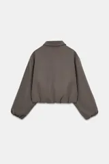 Chaqueta de corte corto y diseño abullonado en color marrón oscuro, con cuello solapa, mangas largas con puños elásticos y cierre frontal con cremallera metálica. Cuenta con bolsillos delanteros de doble vivo.