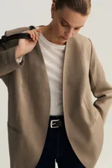 Blazer de sarga sin solapas color marrón, con hombreras, frente abierto, pinzas en la cintura, bolsillos delanteros ribeteados y forro interior.