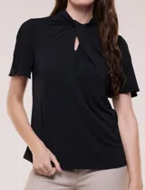 Blusa blanca de corte recto con cuello alto torzado, abertura frontal en gota y mangas cortas con aberturas sobre los hombros.