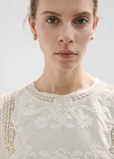 Top blanco de algodón con cuello redondo, detalles bordados, inserciones de encaje y terminaciones festoneadas en mangas y ruedo.