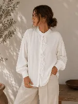 Camisa negra de calce relajado con cuello mao, cierre frontal de botones y detalle de volado vertical en el frente. Presenta mangas largas con puños abotonados.