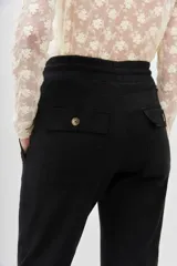 Pantalón tipo babucha de gabardina elastizada, color negro, con cintura elástica ajustable mediante cordón, puños en los tobillos, bolsillos diagonales frontales y bolsillos traseros con solapa y botón.