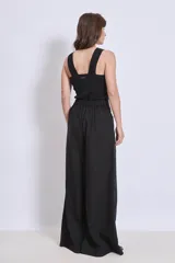 Pantalón negro de corte palazzo con bolsillos laterales y apliques bordados de hojas en color crudo en una pierna.