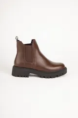Bota estilo Chelsea de caña baja en cuero sintético color marrón, con punta redonda, paneles elásticos laterales y suela track negra con plataforma.