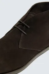 Bota de cordones tipo derby, color marrón oscuro, fabricada en piel con acabado serraje. Tiene plantilla interior de piel, horma redonda y suela fina a contraste.