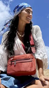 Bandolera de diseño moderno y funcional, confeccionada en nylon color marrón claro. Cuenta con múltiples compartimentos con cierre metálico, herrajes plateados y una correa ancha ajustable con detalle de marca.