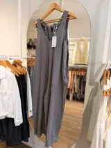 Mono largo de lino color gris, con escote en V, silueta holgada, bolsillos laterales y tirantes anchos con detalle de lazos ajustables en la espalda.