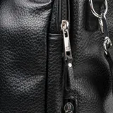 Bolso matero de diseño vertical en color negro, confeccionado en material texturizado símil cuero. Cuenta con doble asa superior, correa ajustable y extraíble para llevar al hombro, y cierre principal. Incluye un aplique metálico con el logo de la marca en el frente.