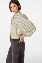 Camisa blanca de viscosa con cuello camisero, mangas largas abullonadas con puños elásticos y cierre frontal con botones. Presenta bordados negros con motivos florales en las mangas.