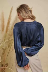 Blusa de satén color azul marino, con cuello mao, cierre frontal de botones y mangas largas con puños elásticos. Presenta detalles fruncidos en los hombros.