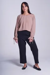 Blusa de manga larga color rosado, con cuello redondo y puños elásticos con volados y lazos decorativos. Presenta un diseño holgado con frunces en el escote.