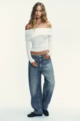 Jeans de tiro medio con diseño baggy barrel, cinco bolsillos y costuras laterales torcidas. Presenta cierre frontal con cremallera y botón metálico.