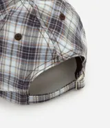 Gorra de aba curva confeccionada en franela de algodón, con diseño a cuadros en tonos gris, celeste y blanco, paneles estructurados y cierre regulable trasero con hebilla metálica.