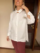 Camisa de corte clásico y calce holgado, color blanco, con cuello camisero, cierre frontal de botones ocultos y mangas largas con puños abotonados.