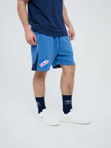 Bermuda deportiva Umbro del Club Nacional de Football, modelo Nexo para hombre, en color azul marino con detalles en rojo y blanco. Cuenta con el escudo del club bordado en la pierna derecha y el logo de Umbro en la izquierda, además de cordón ajustable en la cintura.