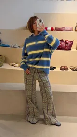 Pantalón de corte recto y tiro medio con estampado geométrico en tonos amarillos, verdes y violetas. Presenta un diseño de líneas verticales que forman cuadros y un patrón repetitivo de letras.