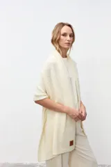 Chal de punto color crudo, con diseño envolvente y textura suave. Presenta un parche de cuero con logo en la parte inferior.