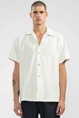 Camisa de manga corta color crema, con cuello camp y calce relajado. Confeccionada en mezcla de algodón y lino, con botones de coco con logo y parche característico de Polonio.