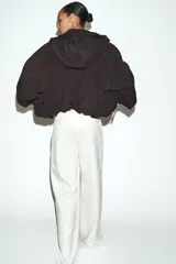 Cazadora de cuello subido con capucha ajustable, manga larga con puños elásticos y bajo elástico. Cuenta con bolsillos delanteros y cierre frontal con cremallera oculta y botones a presión.
