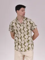 Camisa de manga corta con estampado de hojas color verde sobre fondo beige, cuello solapa y bolsillo en el pecho.