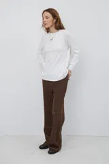 Remera de manga larga en color beige, confeccionada en tejido de punto con costuras a la vista en contraste. Presenta un corte holgado, cuello redondo y un pequeño bordado distintivo en la parte inferior.