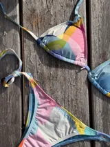 Bikini color dorado brillante, con corpiño triangular de atar al cuello y espalda, con almohadillas desmontables. La bombacha es vedetina con tiras ajustables a los costados.