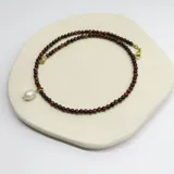 Collar de cuentas de piedra Ojo de Buey de 4 mm con un dije central de perla de río natural y detalles metálicos con baño de oro.