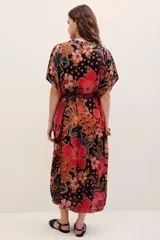Vestido midi de viscosa con estampado floral en tonos rojos, naranjas y negros sobre base oscura. Cuenta con mangas cortas amplias, escote en V con cuello tipo camisero y cierre frontal de botones.