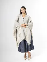 Ruana de punto color beige con sutiles motas multicolores, con bordes terminados en flecos largos.