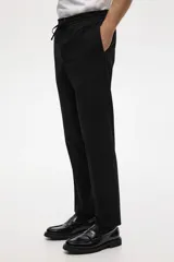 Pantalón tipo jogger de vestir negro, corte slim fit, con pliegues frontales y traseros, cintura elástica con cordón de ajuste y bolsillos laterales y traseros.
