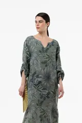 Vestido largo de lino de calce relajado y silueta fluida, con estampa botánica en tonos verdes y azules sobre fondo beige. Cuenta con escote en V y mangas amplias.