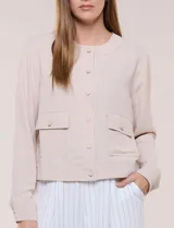 Camperita de tela liviana color beige, de silueta entallada con cuello a la base y abotonadura frontal con botones a tono. Cuenta con dos bolsillos con solapa en el frente, mangas largas con puños abotonados y largo a la cintura.