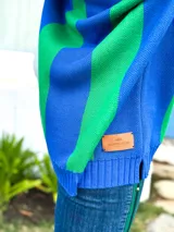 Sweater de punto azul con cuello polo blanco, diseño geométrico en el pecho en blanco y verde, y mangas largas.