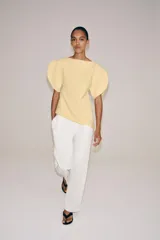 Top amarillo de manga corta abullonada, con cuello barco y bajo asimétrico. Cierre trasero con cremallera oculta.