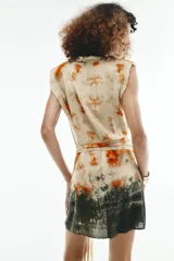 Vestido corto sin mangas de cuello redondo, con estampado tie-dye en tonos beige, naranja y verde oscuro. Presenta un lazo para atar en la cintura y cierre trasero con cremallera oculta.