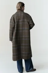 Abrigo largo de corte oversize con estampado de cuadros en tonos marrones y líneas azules. Presenta cuello de solapa, cierre frontal cruzado con botones, mangas largas y bolsillos delanteros con solapa.