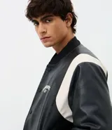 Campera bomber de cuero sintético con diseño bicolor, cuerpo negro y mangas blancas. Presenta cuello, puños y cintura con tejido elástico a rayas, cierre frontal con botones a presión y bordado con la palabra Authentic en el pecho.