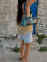 Cartera baguette de cuero marrón con manijas largas y detalle de nudos esféricos de alpaca en la unión de las manijas.