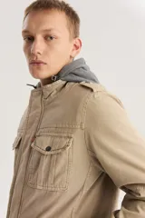 Campera color beige con capucha gris, cierre frontal con cremallera y botones a presión, cuatro bolsillos frontales con solapa y charreteras en los hombros.