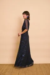 Vestido largo negro con brillos azules, escote en V pronunciado, mangas cortas y amplias tipo capa, y corte en la cintura.