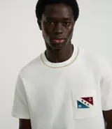 Remera de algodón color crudo, con cuello redondo y manga corta. Presenta un bolsillo en el pecho con estampa náutica y lettering "M.R.F.".