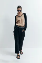 Pantalón negro de corte recto con bolsillos laterales y bordado en contraste blanco en cintura y bolsillos.
