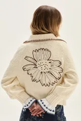 Cardigan de punto color crudo con textura, cuello camisero con borde en contraste, mangas largas con puños acampanados y detalle de bordado floral en la espalda.