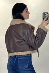 Campera tipo aviador de cuero sintético marrón con interior y detalles de corderito beige. Presenta cierre frontal cruzado, cuello solapa amplio, puños con corderito y cinturón ajustable en la cintura con hebilla metálica.