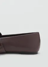 Zapato plano estilo Mary Jane color marrón, confeccionado en piel de ovino, con punta fina y tira en el empeine con hebilla metálica plateada.