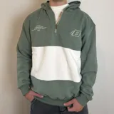 Canguro con capucha y cierre frontal parcial, de diseño color block en verde y blanco. Presenta bordado de la marca Duxon en el pecho y detalles gráficos en el lado derecho.