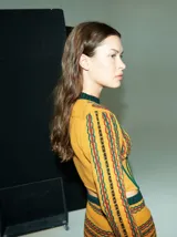 Top tejido de punto color mostaza con rayas horizontales en verde y rojo. Presenta cuello redondo, mangas largas ajustadas, hombreras y un corset integrado con rayas verticales en verde.